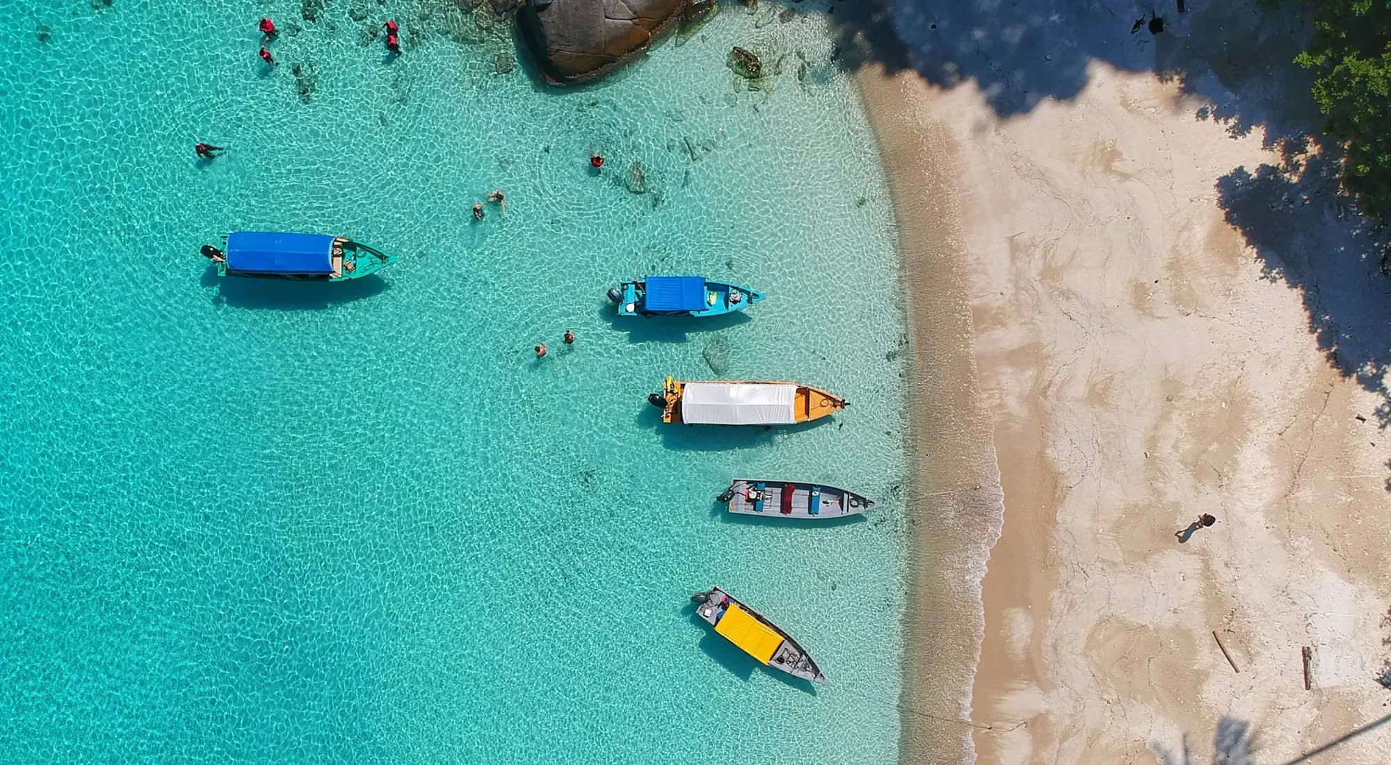 Longboats moored in turquoise water off a white-sand beach, seen from above